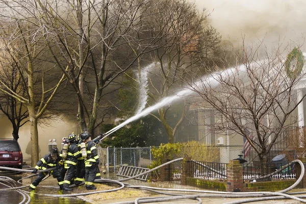 Bombeiros no trabalho apagando um incêndio em casa — Fotografia de Stock