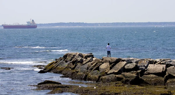 岩が多い防波堤、背景にボートで若い男と — ストック写真