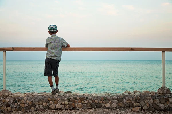Menino em pé no cais ao entardecer olhando para o mar Imagem De Stock
