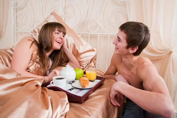 Homem e mulher felizes tendo pequeno-almoço de hotel de luxo na cama juntos — Fotografia de Stock