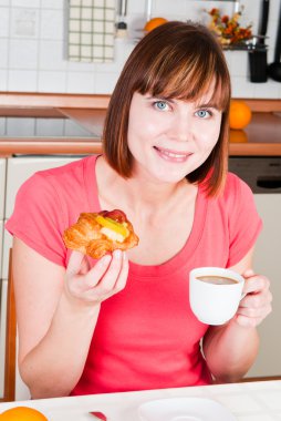 Young woman enjoying a cup of coffee and sweet bun with fruits