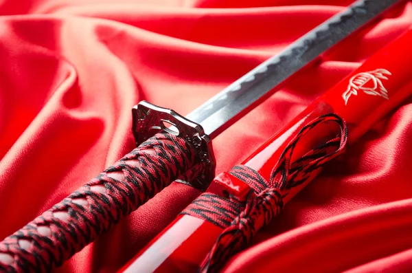 Japon kılıcı takana kırmızı saten zemin üzerine — Stok fotoğraf