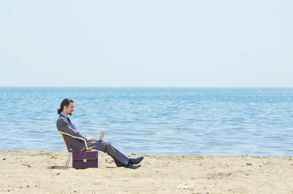 Бизнесмен, работающий над ноутбуком на берегу моря — стоковое фото