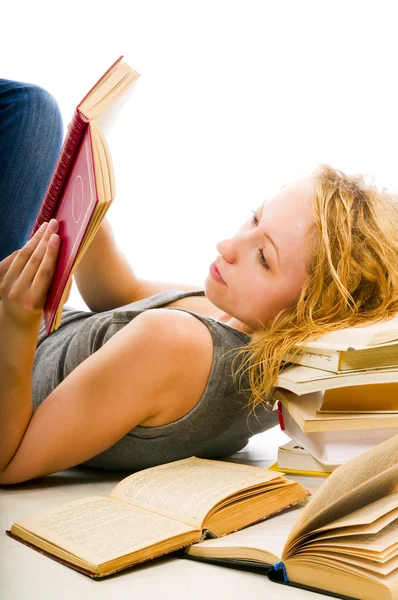 A girl reads a book resting head on pile of books — Stock Photo, Image