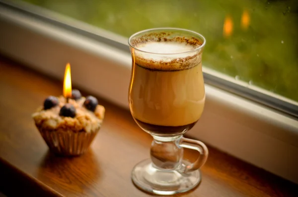 Сoffee latte and a lit candle at rainy window — Stock Photo, Image