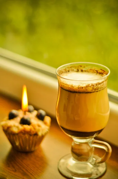 Сoffee latte and a lit candle at rainy window — Stock Photo, Image