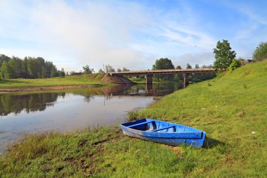 Wooden boat on river coast near villages clipart