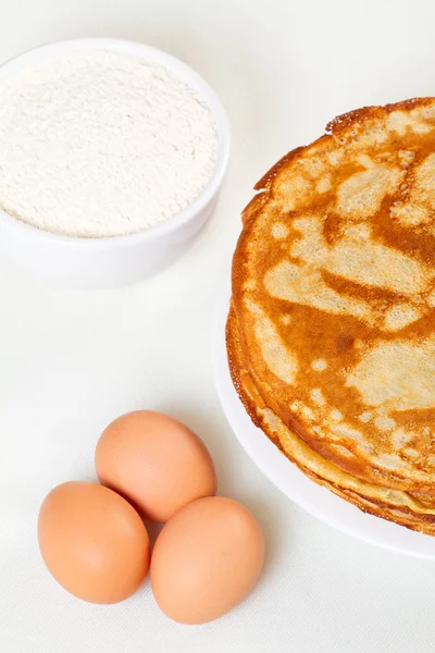 Tumpukan pancake dengan beberapa tepung dan telur di latar belakang putih — Stok Foto