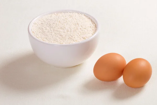Huevos y harina de trigo en un plato sobre fondo blanco — Foto de Stock