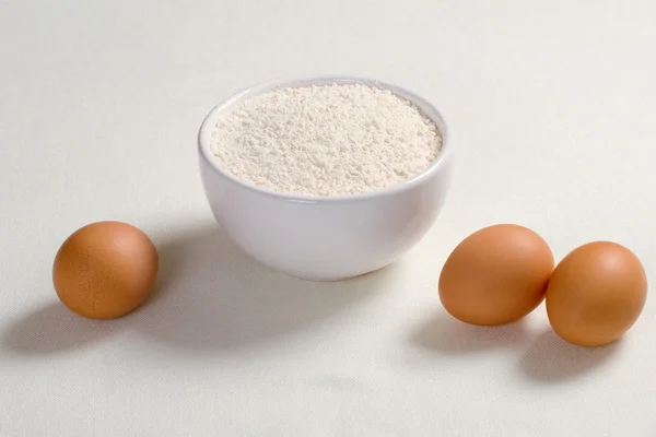 Яйца и пшеничная мука в тарелке на белом фоне — стоковое фото