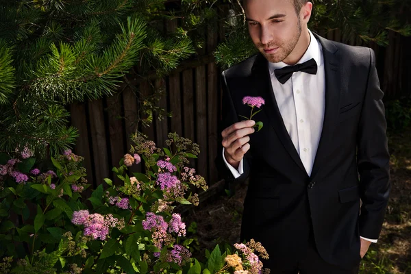 Portrait of young beautiful fashionable man against summer garden. — Stock Photo, Image