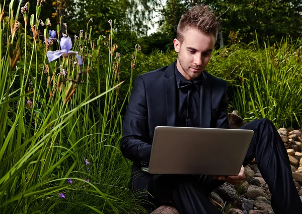 Молодой красивый модный мужчина с ноутбуком против летнего сада . — стоковое фото