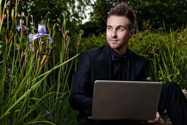 Young beautiful fashionable man with notebook against summer garden. — Stock Photo, Image