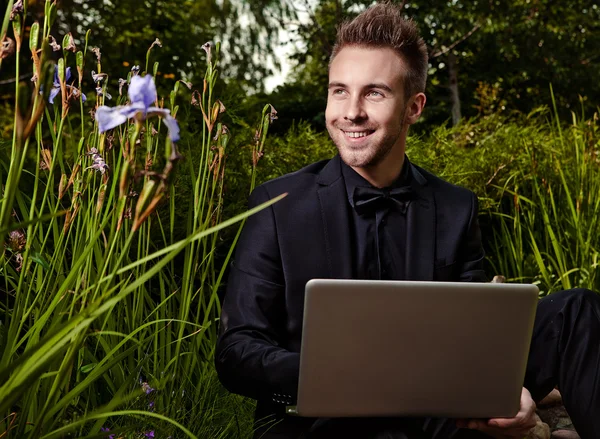 Молодой красивый модный мужчина с ноутбуком против летнего сада . — стоковое фото