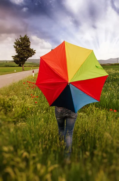 Meisje met paraplu op veld met dramatische hemel — Stockfoto