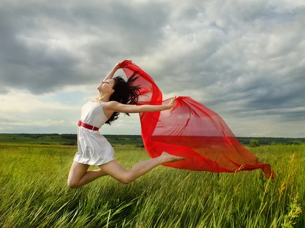Brunette girl jumping with red fabric in summer day — Stock Photo, Image