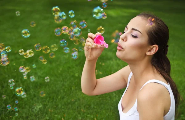 Beautiful young brunette girl blowing soap bubbles — Stock Photo, Image