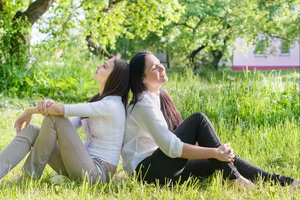 Yeşil çimenlerin üzerinde oturarak iki kız — Stok fotoğraf