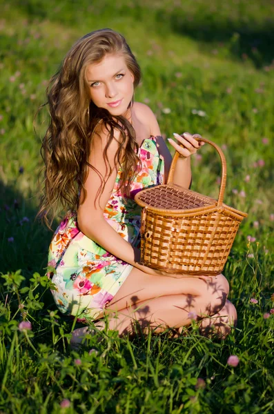Dziewczyna siedzi w trawie z koszem na zachód słońca — Zdjęcie stockowe