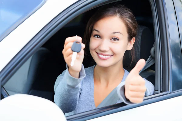 Chica feliz en un coche mostrando una llave y el pulgar hacia arriba gesto —  Fotos de Stock