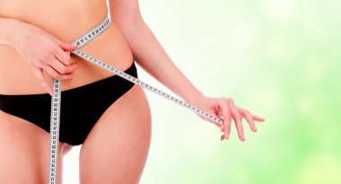 Girl taking measurements of her body, green blurry background. clipart