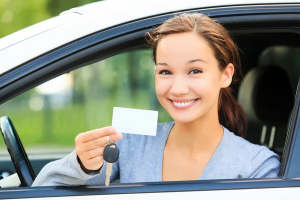 Дівчина в машині, що показує ключ і порожню білу карту — стокове фото
