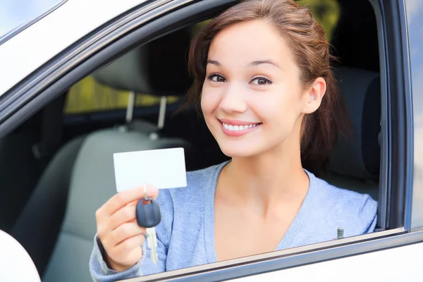 Chica en un coche mostrando una llave y una tarjeta blanca vacía — Foto de Stock