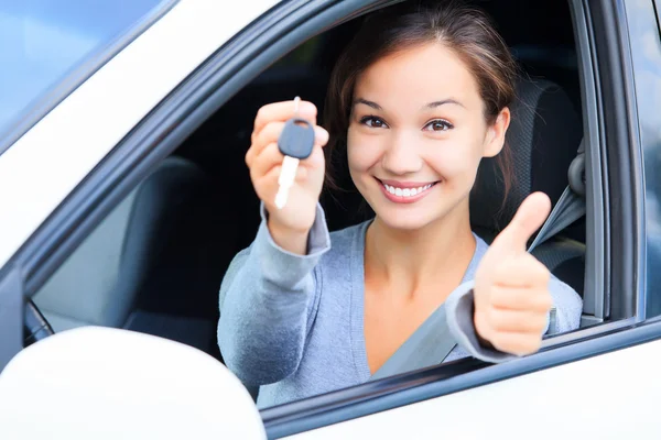 Счастливая девушка в машине показывает ключ и большой палец вверх жест — стоковое фото