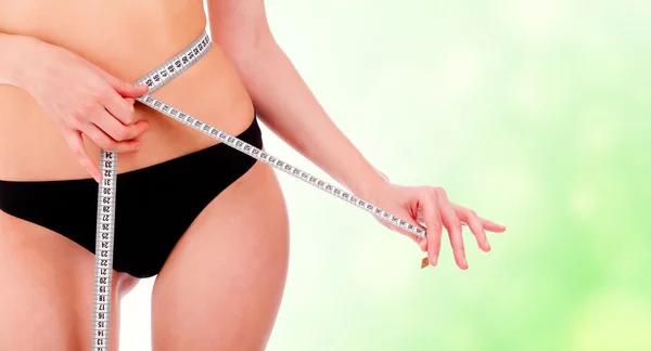 Meisje dat neemt metingen van haar lichaam, groene onscherpe achtergrond. — Stockfoto