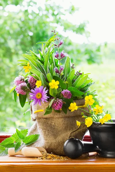 Sack with bouquet of healing herbs and flowers, mortar and pestle on windowsill — Stock Photo, Image