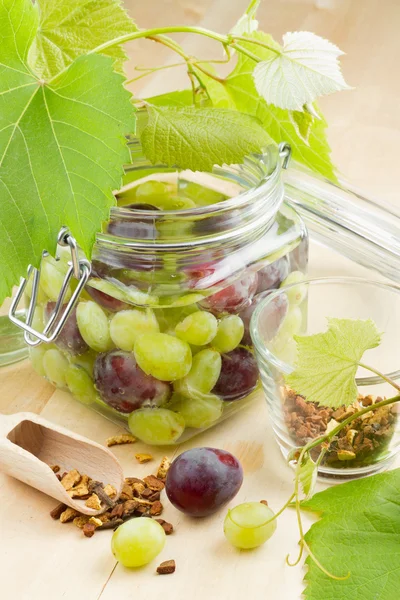 Tarro de vidrio con uvas enlatadas, hojas de uva y especias en mesa de madera — Foto de Stock