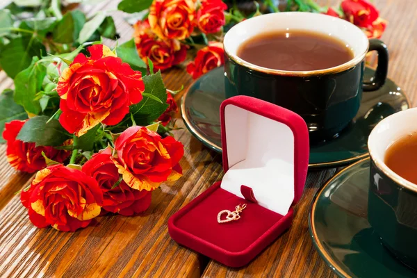 Arany ékszerek, csésze tea és a rózsa csokor — Stock Fotó