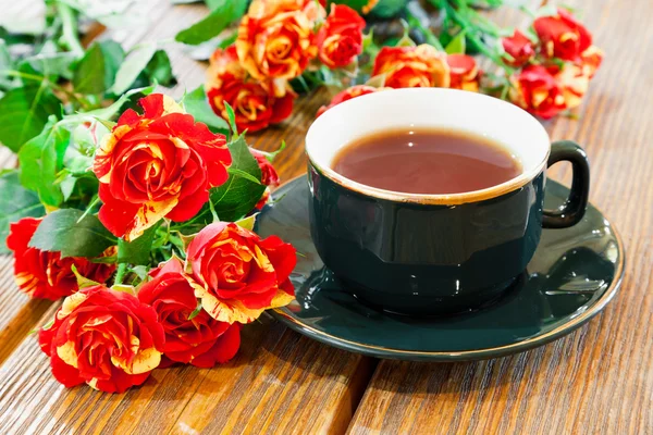 Чашка чая и букет роз на деревянном столе — стоковое фото