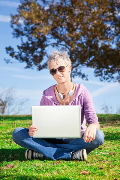 Молодая женщина с ноутбуком сидит на траве — стоковое фото