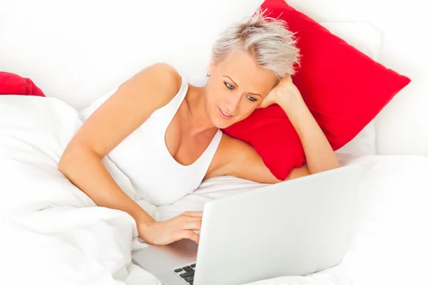 Muchacha atractiva acostada en la cama con el ordenador portátil —  Fotos de Stock