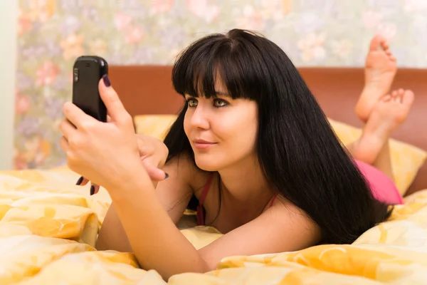Lachende jonge vrouw met mobiele telefoon in bed — Stockfoto