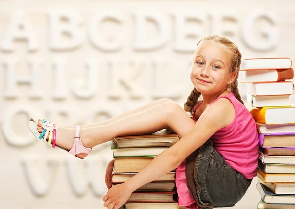 Kleines Schulmädchen sitzt auf Büchern — Stockfoto