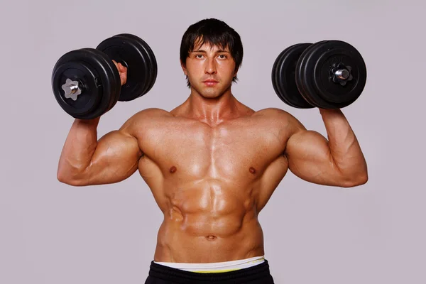 Porträt eines Muskelmannes auf grauem Hintergrund mit Hanteln — Stockfoto