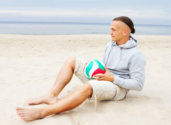 Portrait of man sittin on the beach in a coat with ball — Stock Photo, Image