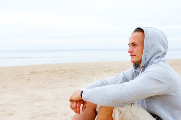 Portrét člověka sedí na pláži v kabátě — Stock fotografie