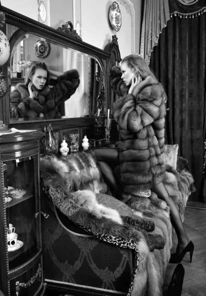 Frau im Pelzmantel am Spiegel in luxuriösem klassischem Interieur — Stockfoto