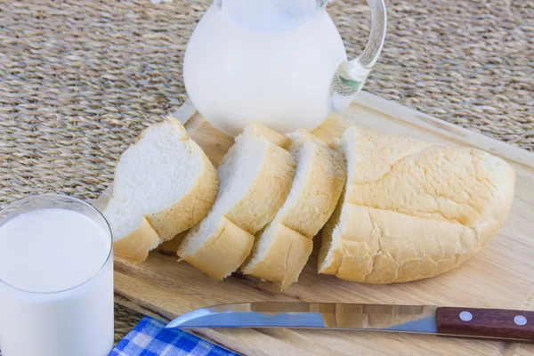 Fresh cut long loaf and milk in a jug — Stock Photo, Image