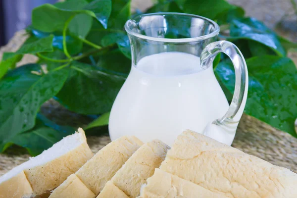 Fresh cut long loaf and milk in a jug — Stock Photo, Image