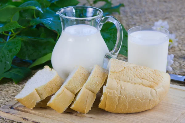 stock image Fresh cut long loaf and milk in a jug