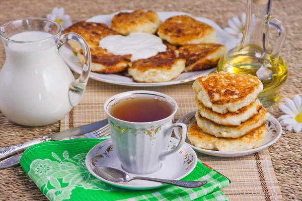 Kopp med te, ostmassa pannkakorna på ett fat och mjölk — Stockfoto