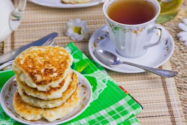 Kopp med te, ostmassa pannkakorna på ett fat och mjölk — Stockfoto