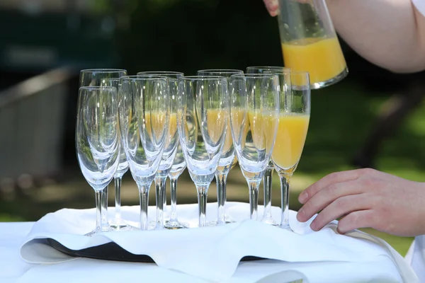 Wylewanie soku pomarańczowego na flety szampana — Zdjęcie stockowe