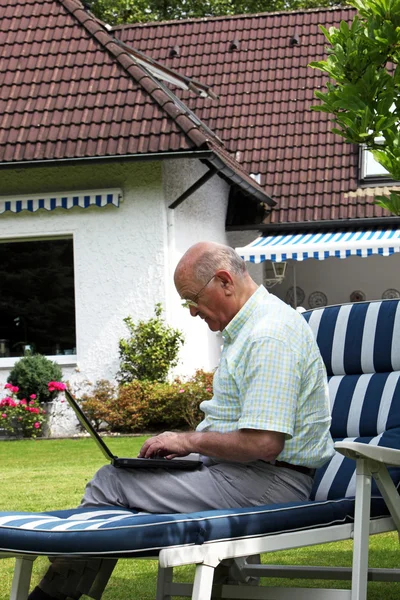 Пожилой человек печатает на открытом воздухе на ноутбуке — стоковое фото