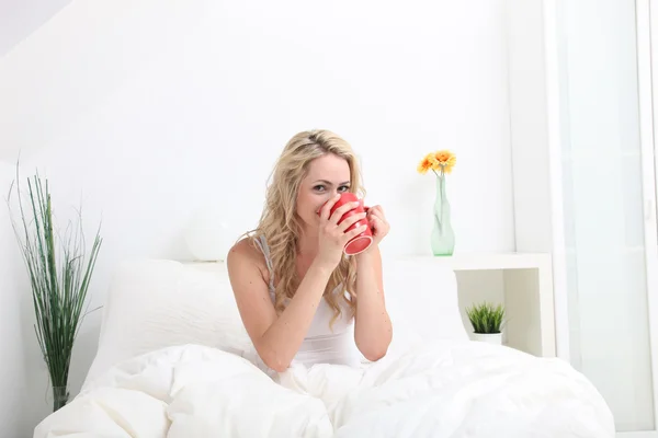 コーヒーを楽しんでベッドに座っている女性 — ストック写真