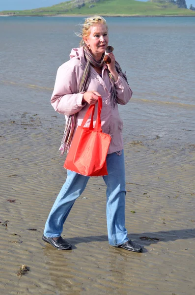 Žena chodí s červenou taškou na pláži — Stock fotografie
